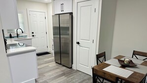 A modern kitchen with white cabinetry, a stainless steel refrigerator, and a dining area with a wooden table and chairs.