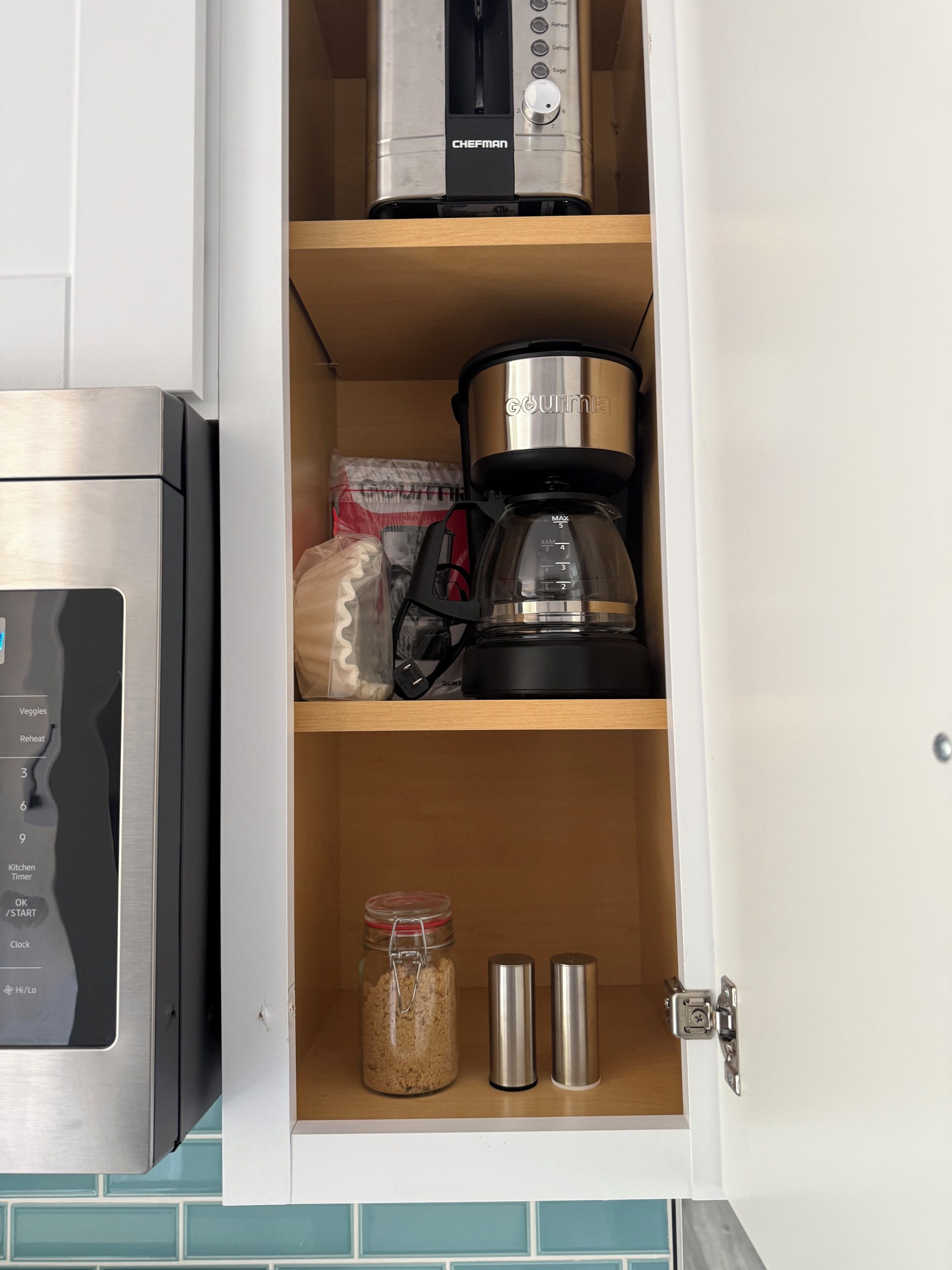 A kitchen cabinet with a coffee maker, a food processor, and a jar of spices.