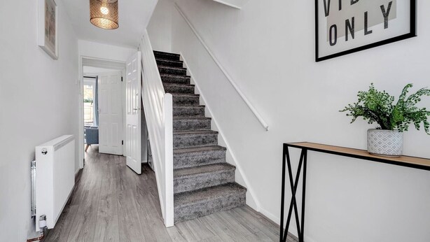 Una escalera moderna con acabado de madera, barandilla blanca y un letrero en la pared que dice "GOOD VIBES ONLY".