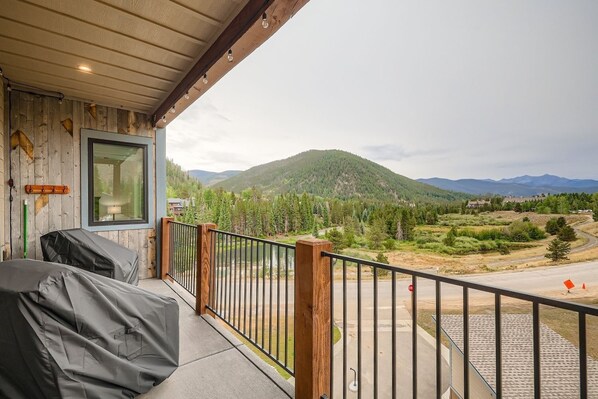 Un balcon donnant sur un paysage montagneux, un plafond en bois et une fenêtre avec des stores.