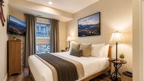 A hotel room with a bed, two bedside lamps, a view of Park City, Utah, and a window with curtains. - Peaceful Lift Line Condo 207 3 Bedroom Condo (Park City)