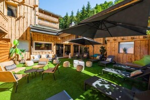 A wooden cabin with a patio area featuring outdoor furniture and a large umbrella. - Hotel la Chaudanne (Meribel)