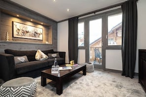 Een moderne woonkamer met een donkerbruine bank, een salontafel en een groot raam met gordijnen.