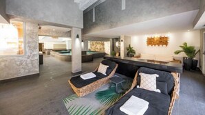 A modern spa area with wicker lounge chairs, a reception desk, and a stone wall. - Hotel la Chaudanne (Meribel)