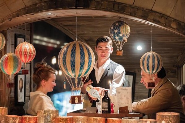 A bar setting with a counter, hanging hot air balloons, and a menu. - Hotel la Chaudanne (Meribel)