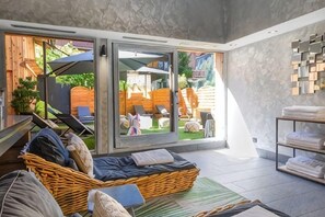A modern interior with a wicker sofa, a glass door leading to an outdoor area, and a tiled floor. - Hotel la Chaudanne (Meribel)