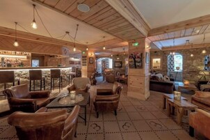 Un intérieur chaleureux avec des poutres en bois, un coin bar et différents espaces pour s’asseoir.