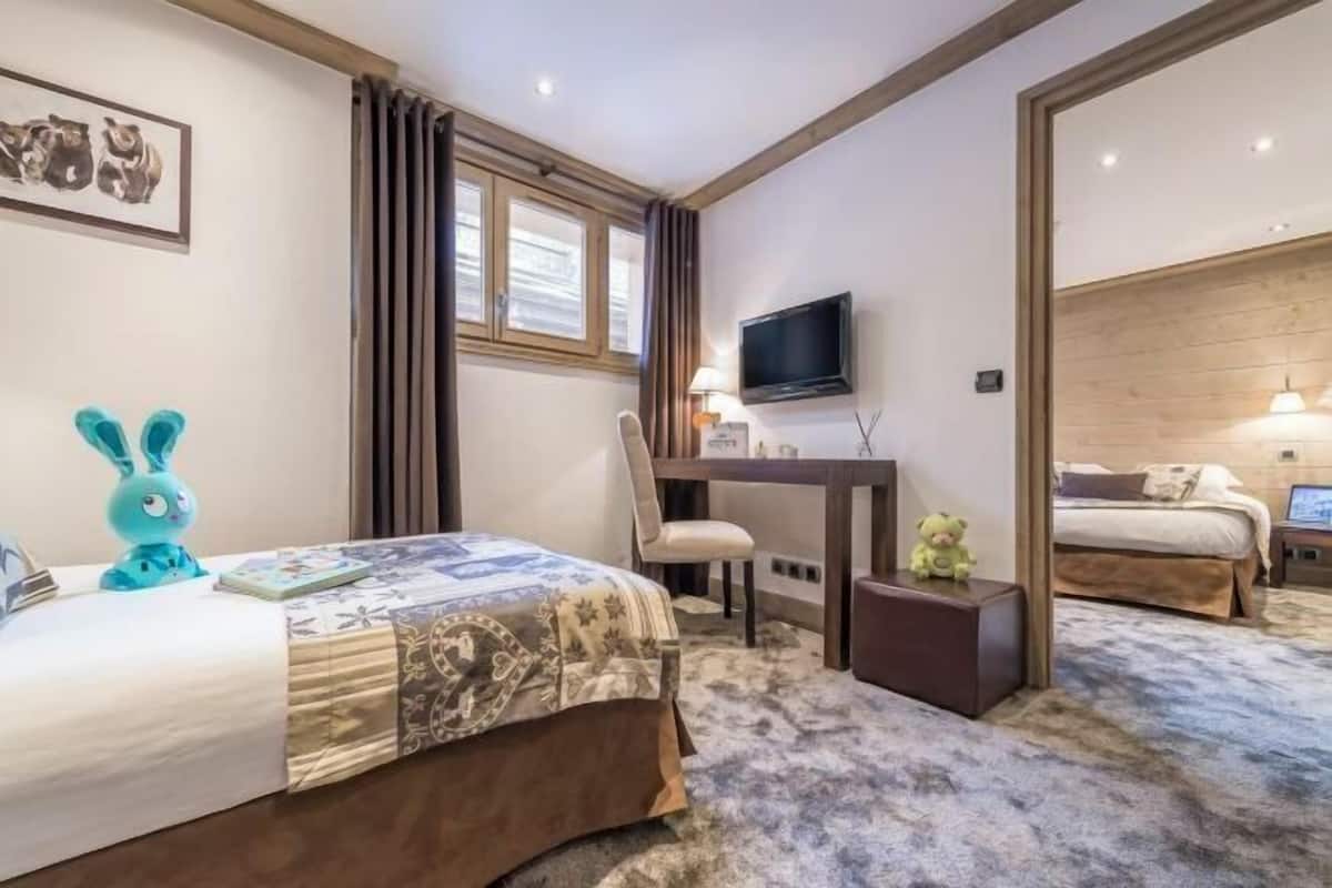 Una habitación de hotel con cama, escritorio, televisor y ventana con cortinas.