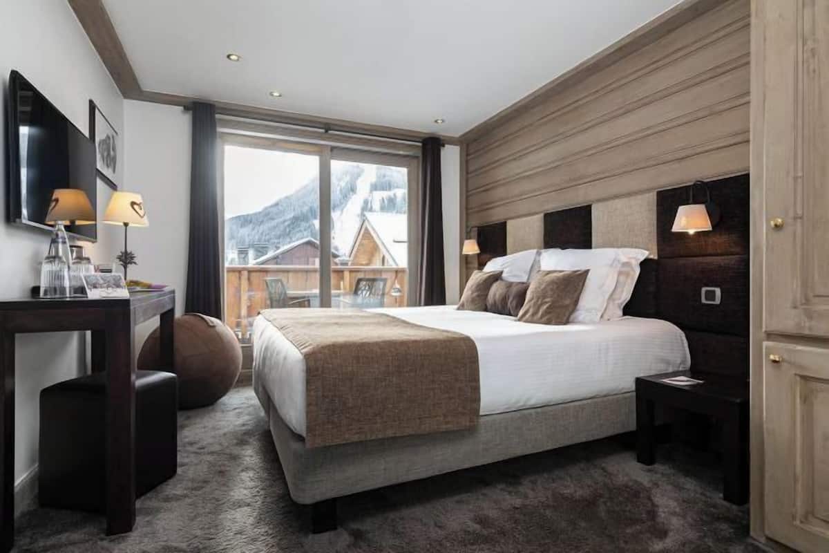 Un dormitorio con cama, mesitas de noche, un escritorio y una ventana con vistas a las montañas.