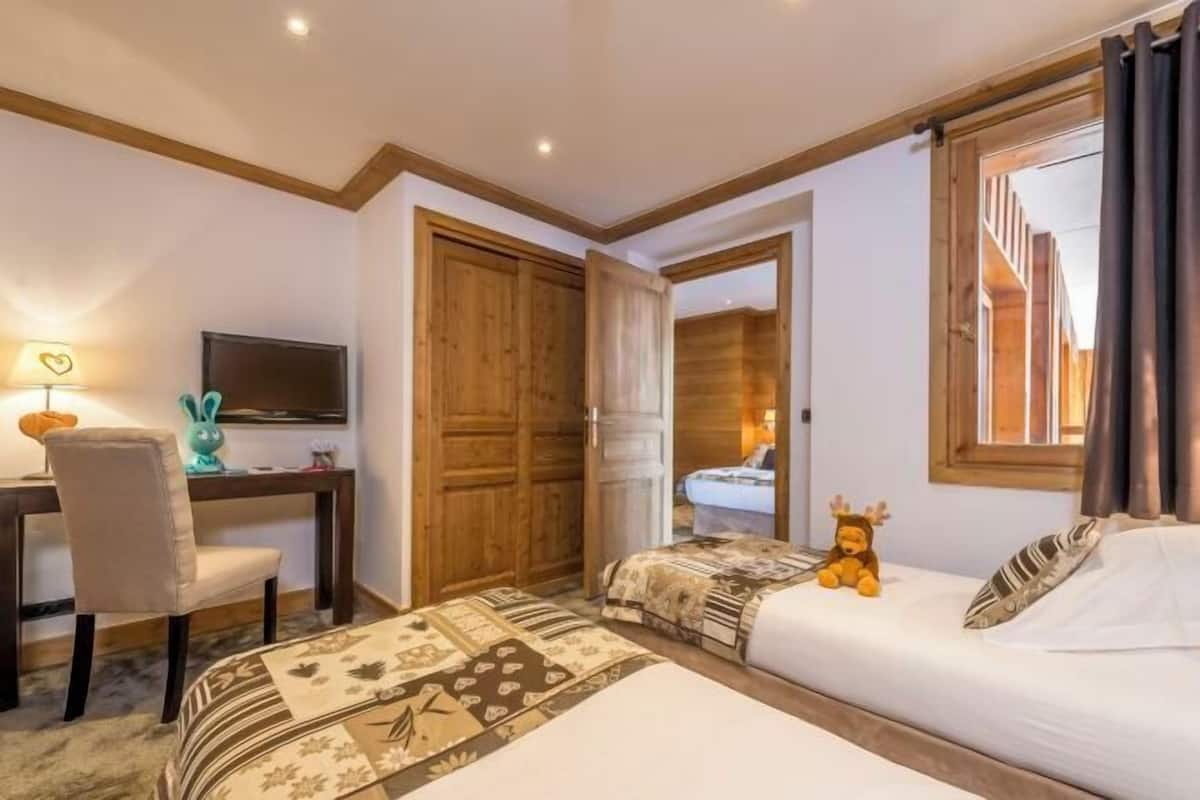 Una habitación de hotel con dos camas, un escritorio con silla, televisión y ventana con cortinas.