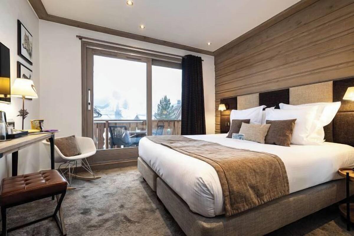 Habitación de hotel con una cama grande, un escritorio con silla, vistas por un ventanal y un balcón.