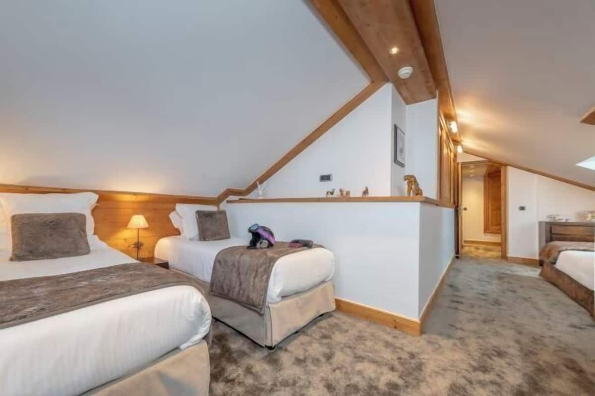 Un dormitorio acogedor en el ático con dos camas, techo de madera y un pequeño escritorio.