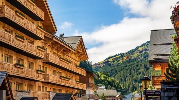 A traditional wooden building with multiple balconies, a stone foundation, and a view of a forested hillside. - Hotel la Chaudanne (Meribel)