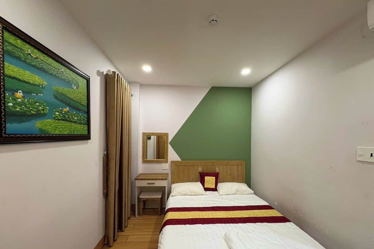 A bedroom with a bed, a desk, a chair, a mirror, and a painting on the wall.