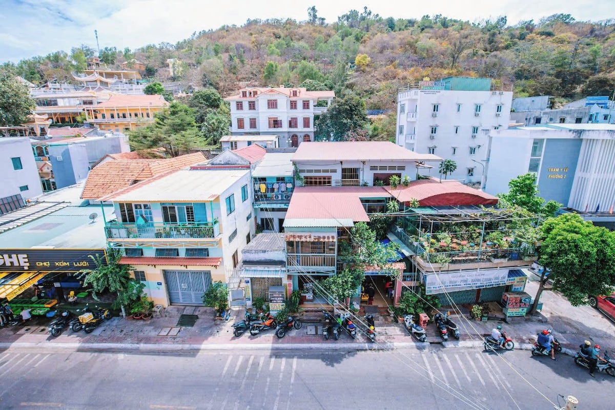 A multi-story building with a commercial ground floor, a parking area, and a hilly backdrop.