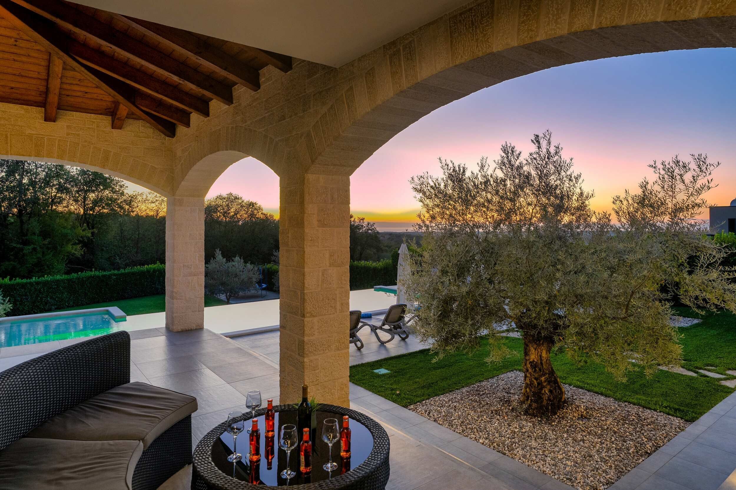 A covered outdoor area with a pool, seating, and a view of the sunset.
