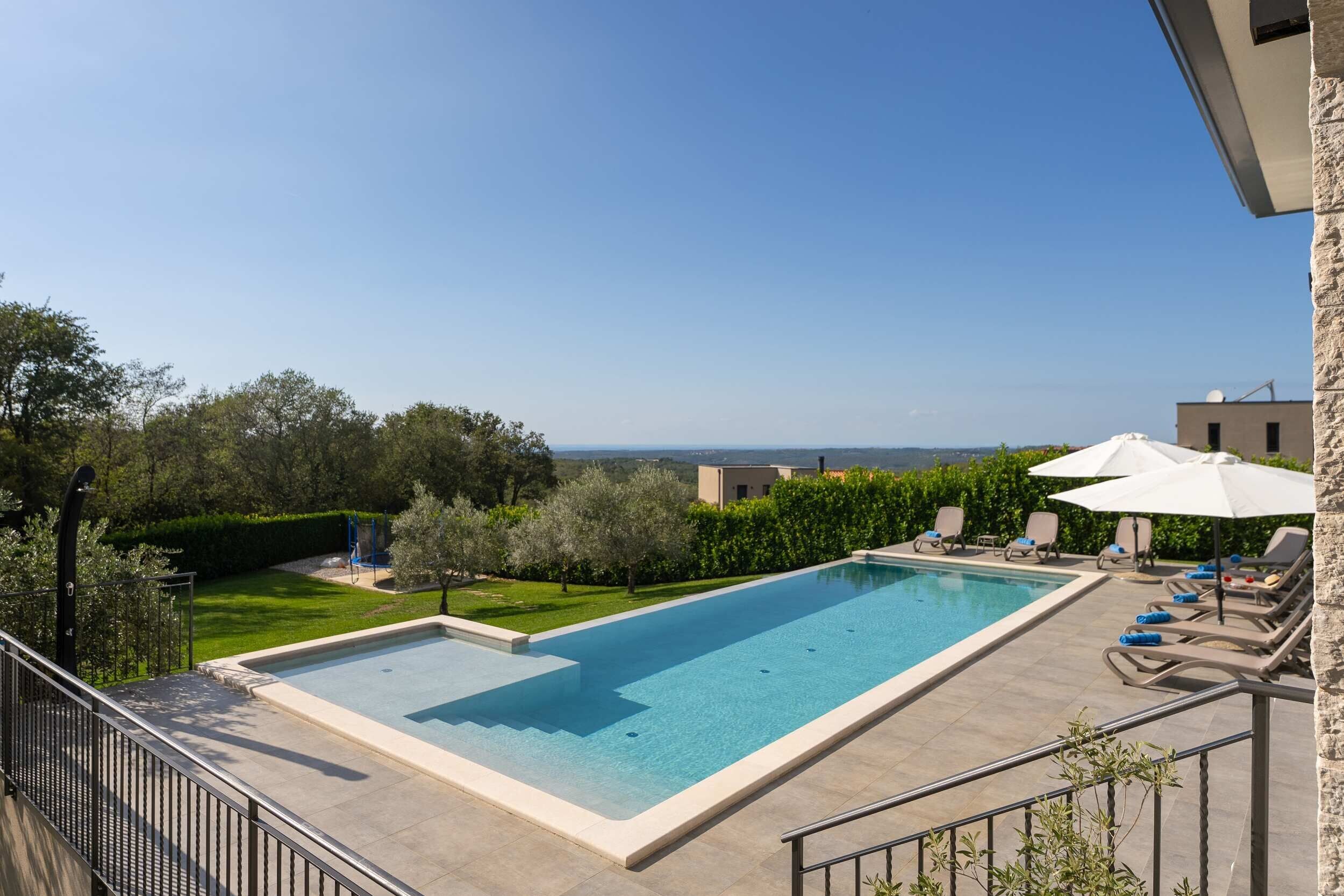 Una piscina rectangular con vistas al mar, rodeada por un patio con sillas de descanso y sombrillas.