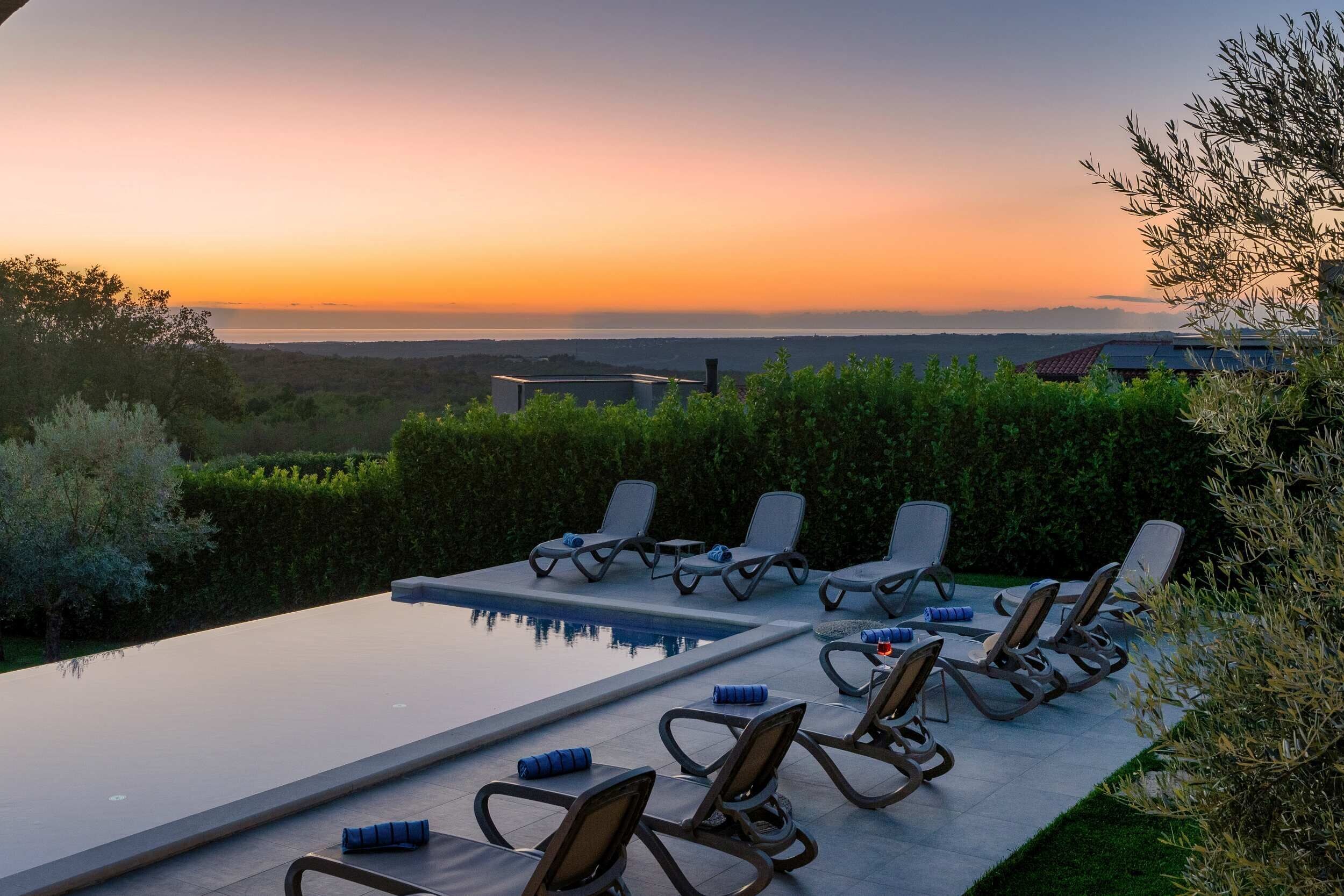 An infinity pool with lounge chairs and a view of the sunset over the ocean.