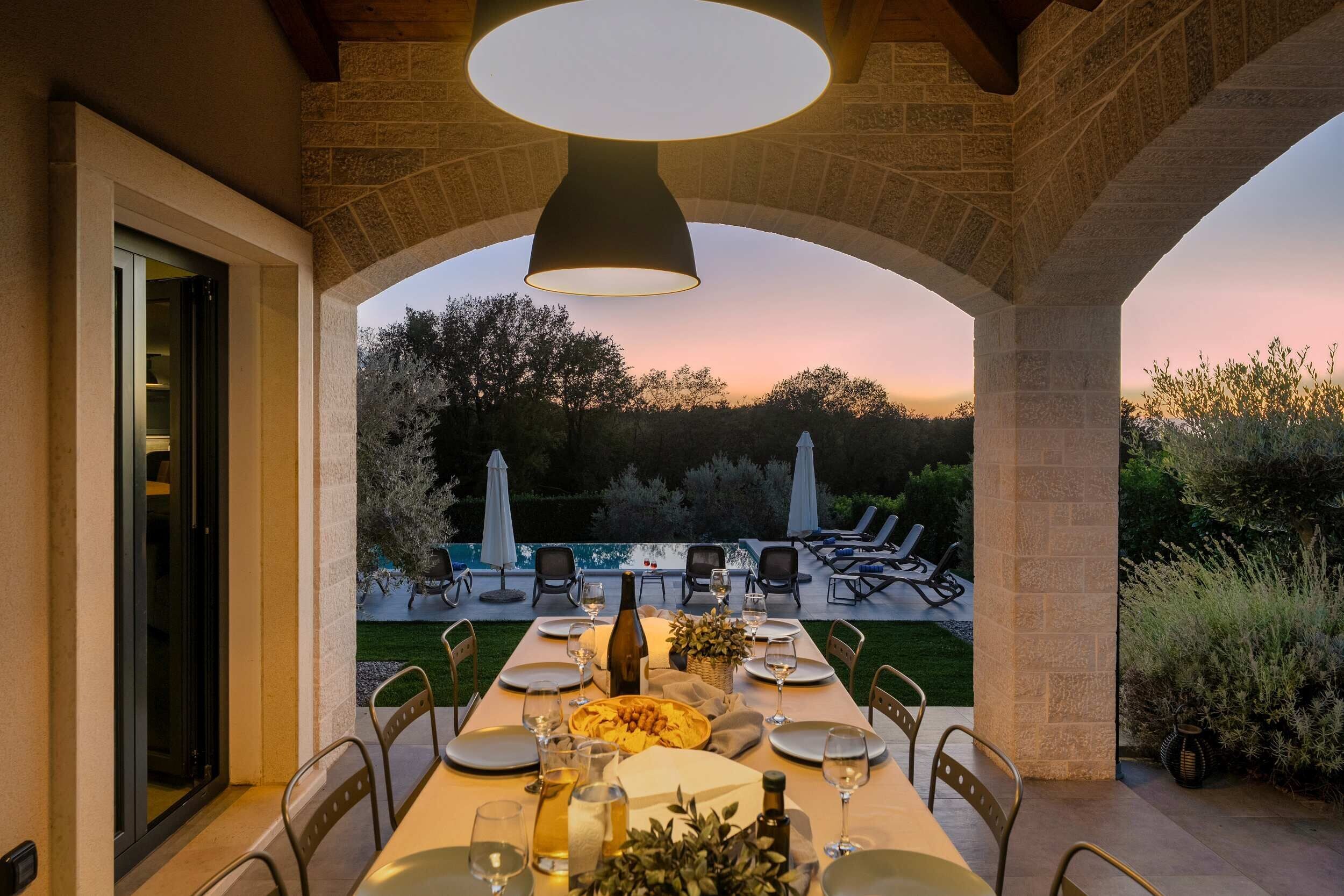 An outdoor dining area with a table set for four, overlooking a pool and garden.