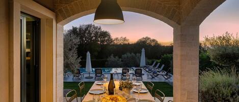 Zona d'esmorzar a l'aire lliure amb taula preparada per a quatre persones, amb vista a una piscina i un jardí.