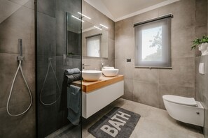 A modern bathroom with a glass-enclosed shower, a wooden vanity with a white sink, and a toilet.