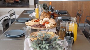 Et spisebord dækket med tallerkener, glas og forskellige spiser, herunder brød, ost og tomater.