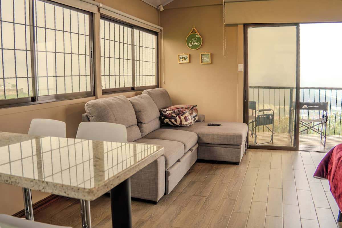 Un espacio de estar con un sofá modular, una mesa de comedor y un balcón con sillas.