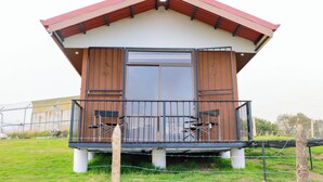 A small, single-story building with a red roof and a large sliding glass door. It has a balcony with metal railings and two chairs. - Cabañas La Montañuela (Llano Grande)
