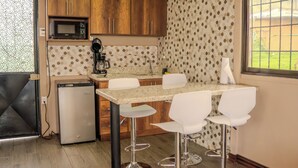 A compact kitchen with wooden cabinets, a microwave, a coffee maker, and a small refrigerator. There is a dining area with a table and four chairs. - Cabañas La Montañuela (Llano Grande)