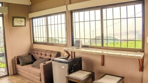A room with a sofa, a small table, a TV, and a window with a view of a green landscape. - Cabañas La Montañuela (Llano Grande)