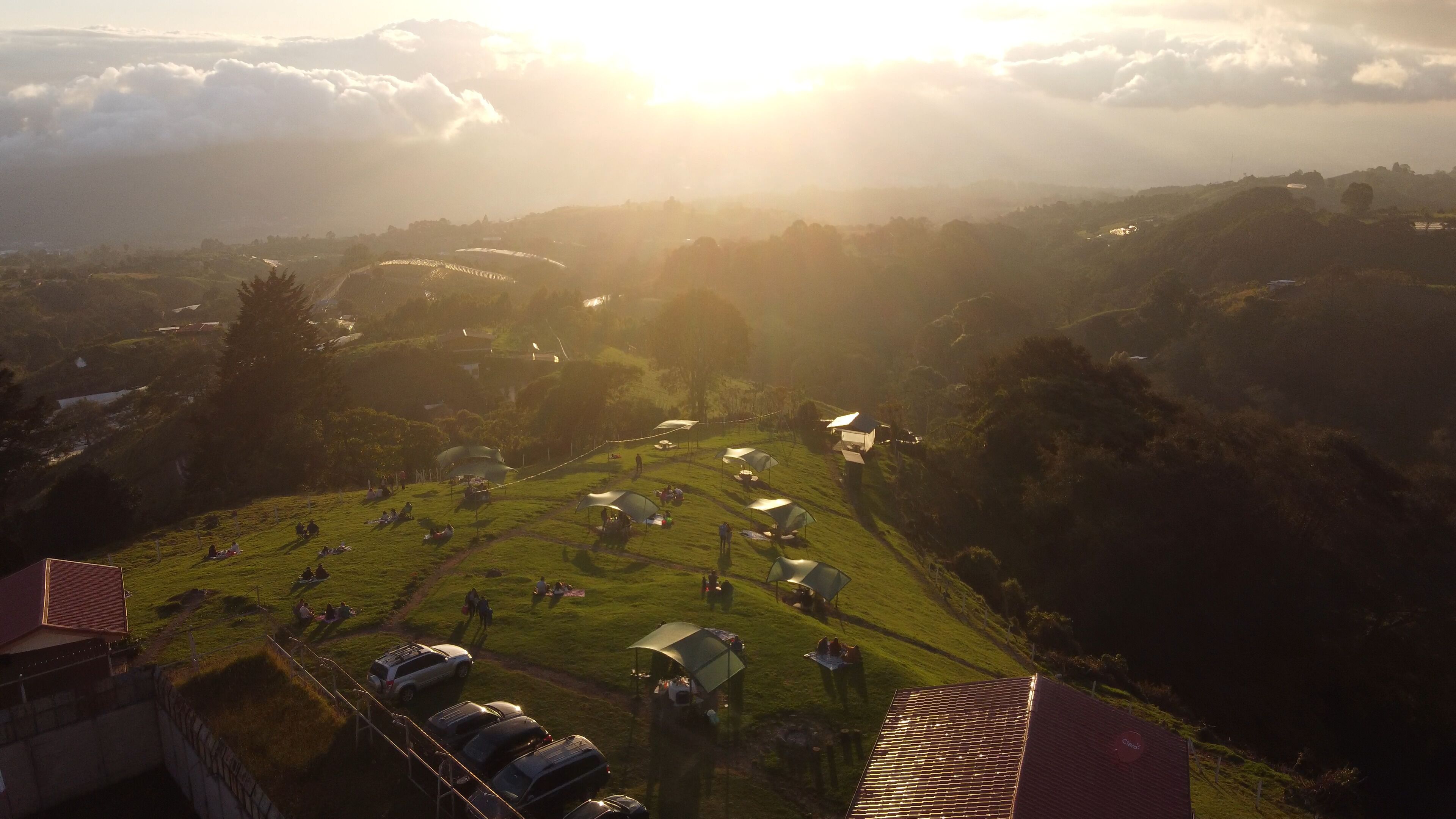 A rural landscape with tents and cars, suggesting a campsite or outdoor event.
