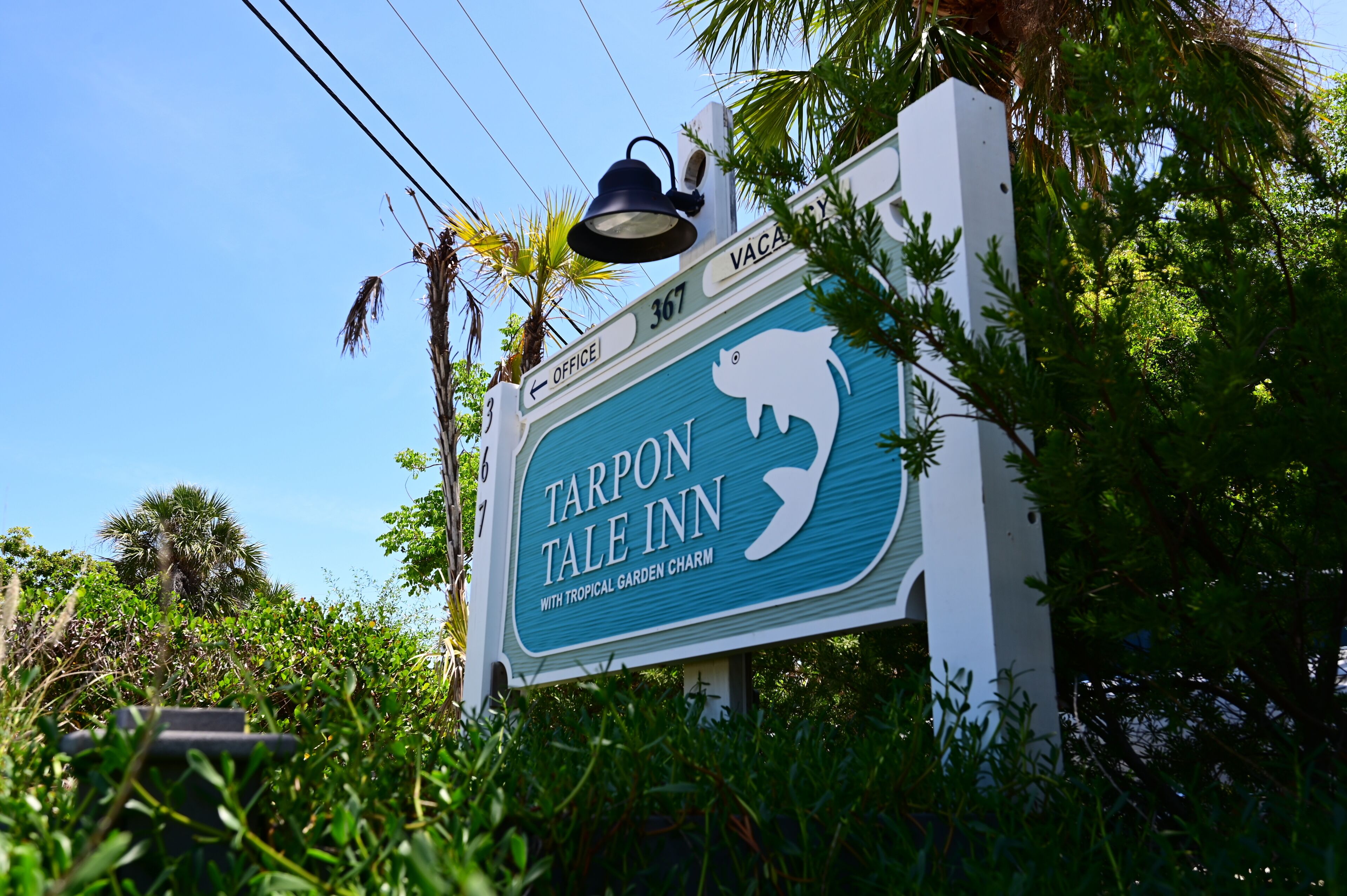 En skylt för Tarpon Tale Inn, med en tropisk trädgård som ger platsen en speciell charm.