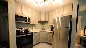 A modern kitchen with stainless steel appliances, light-colored cabinets, and a tiled floor.
