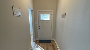 Un couloir doté d’un plancher en bois, une porte avec une fenêtre et un luminaire suspendu.