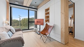 Een moderne kamer met een groot raam, een bank, een leren fauteuil en een bordje 'GUEST READY'.