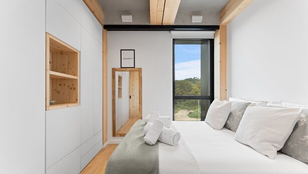 Een moderne slaapkamer met een groot bed, een houten garderobe en uitzicht op de omgeving door een groot raam.