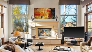 Uma sala de estar com lareira, janelas amplas, televisão e um quadro na parede.