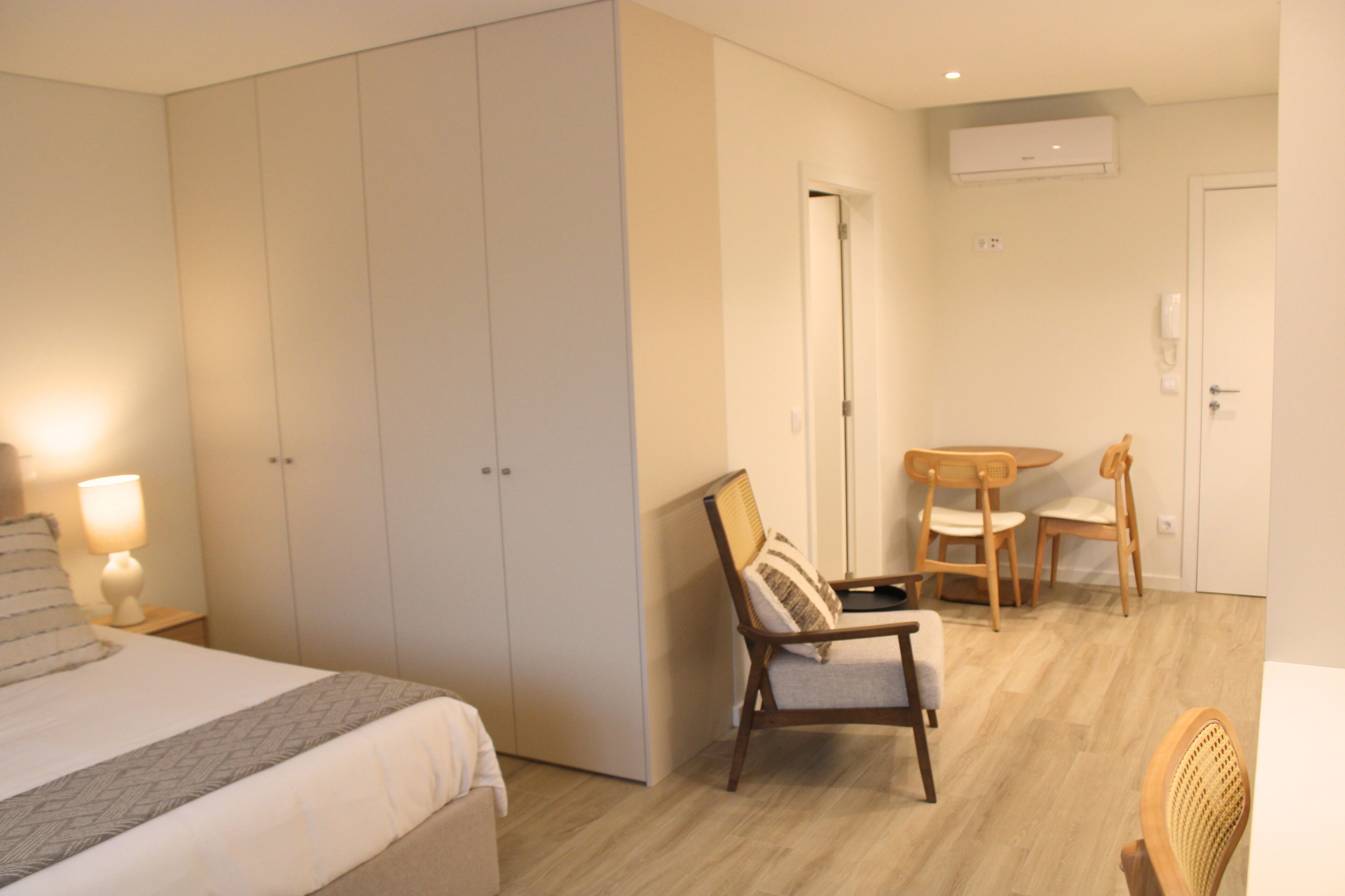 A hotel room with a bed, a chair, a small table, and a wardrobe.