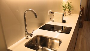 A modern kitchen with a stainless steel sink, a black induction cooktop, and a white countertop. - ma-la studios Guimarães 102 (Guimarães)