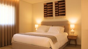 A neatly made bed with a headboard, two bedside lamps, and a large window with curtains. - ma-la studios Guimarães 102 (Guimarães)