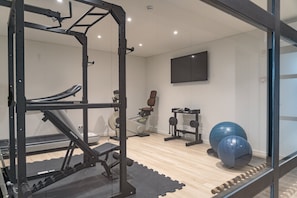 Une salle de sport équipée de matériel d’exercice, avec un téléviseur fixé au mur et un plancher en bois.