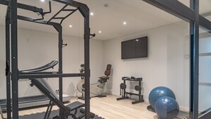 Un gimnasio con equipo de ejercicio, un televisor montado en la pared y piso de madera.