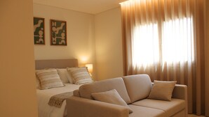 A hotel room with a bed, a sofa, and a large window with curtains.