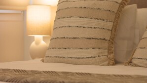 A bed with striped pillows and a textured blanket, a bedside lamp, and a wall fan. - ma-la studios Guimarães 101 (Guimarães)