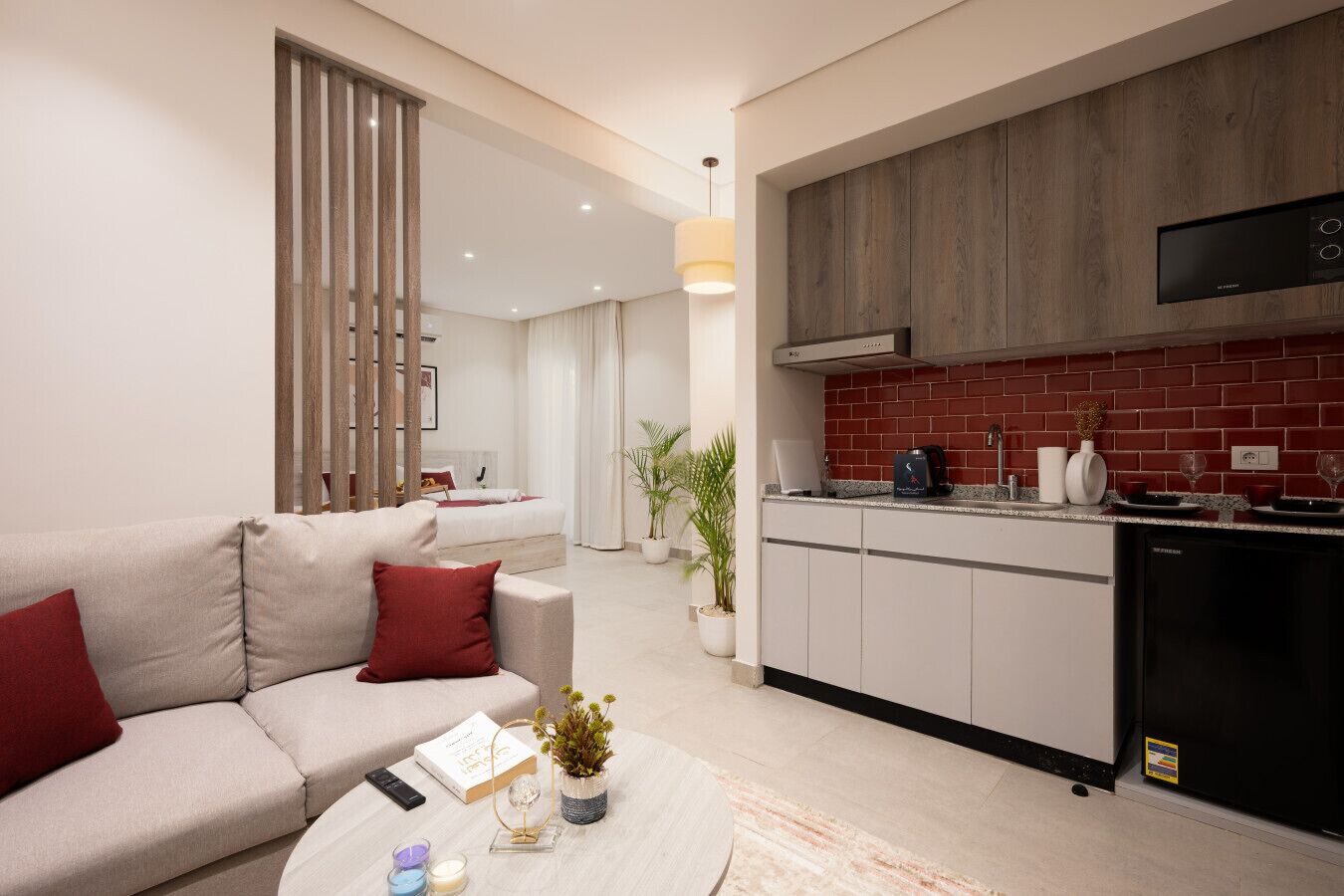 Ein modernes Wohnzimmer mit einer Couch, einem Couchtisch und einer Küchenzeile mit roter Spritzschutzwand und weißen Schränken.