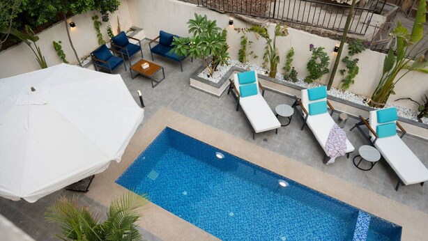 Une piscine extérieure entourée de plantes et d’un mur blanc, avec des chaises longues et des parasols.