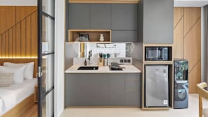 A compact kitchen with a sink, microwave, and refrigerator, adjacent to a bed with a wooden headboard. - Levora by Kozystay - Nusa Dua (Nusa Dua)