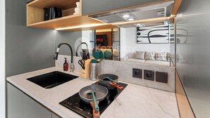 A modern kitchen with a built-in stove, a sink, and wooden shelves above. - Levora by Kozystay - Nusa Dua (Nusa Dua)
