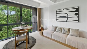 A modern living room with a large window, a dining area, and a sofa. - Levora by Kozystay - Nusa Dua (Nusa Dua)