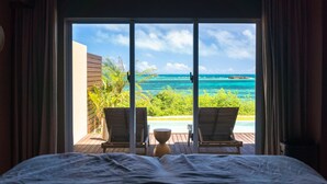 Un dormitorio con una cama, vista al océano, dos sillones y una mesita.
